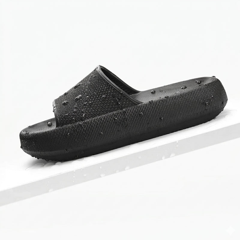 Ein schwarzer, wasserfester Slappys - Original Slipper mit Wassertropfen auf einer weißen, schrägen Oberfläche.